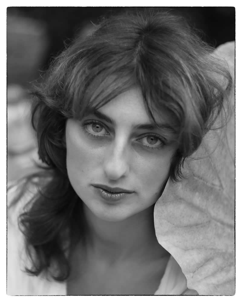 Black and white close-up portrait of a woman looking directly at the camera, with soft light, expressive eyes, and a gentle, intimate mood.