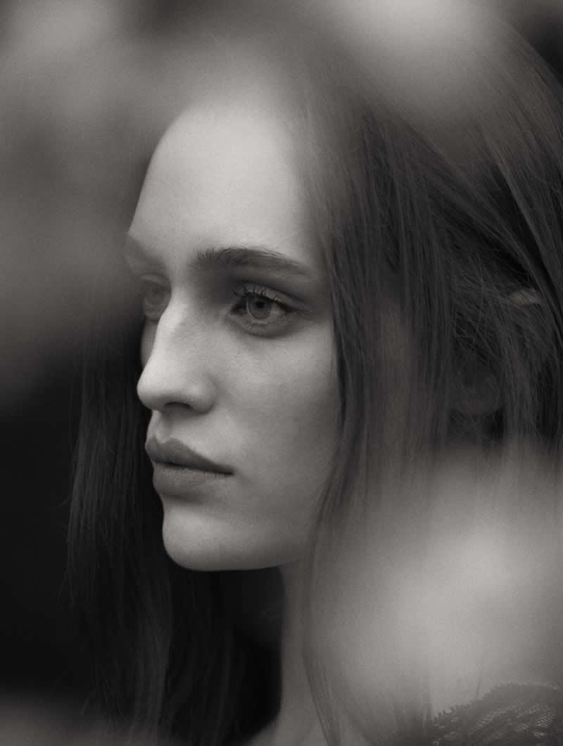 Soft-focus black and white portrait of a woman in profile, partially obscured by blurred foreground elements, creating a dreamy and introspective atmosphere.