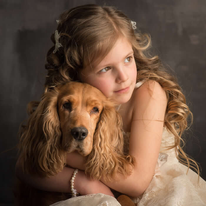 A young girl softly embraces a golden cocker spaniel, resting her cheek against the dog&rsquo;s head, captured in warm studio lighting, expressing innocence, tenderness, and a deep emotional bond between child and animal.