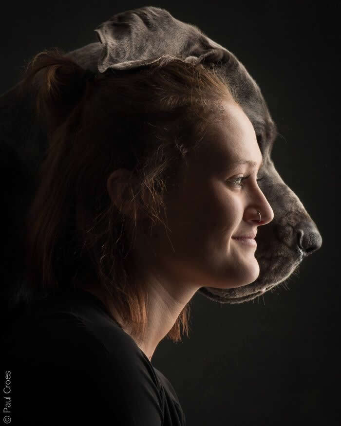 A side-profile portrait of a woman and a large dog aligned closely behind her, both facing the same direction, captured in soft studio lighting, symbolizing unity, companionship, and a shared presence.