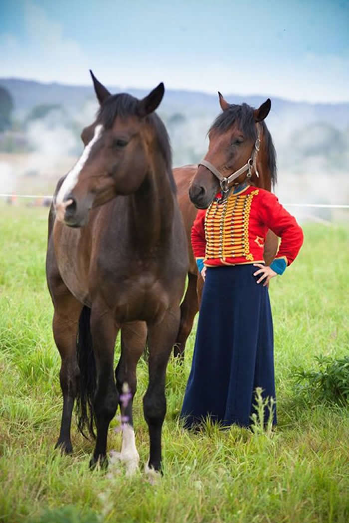 A perfectly timed forced-perspective photo of a brown horse standing in front of a person in a red hussar-style jacket, making it look as though the horse has a human body and is standing upright in a grassy field.