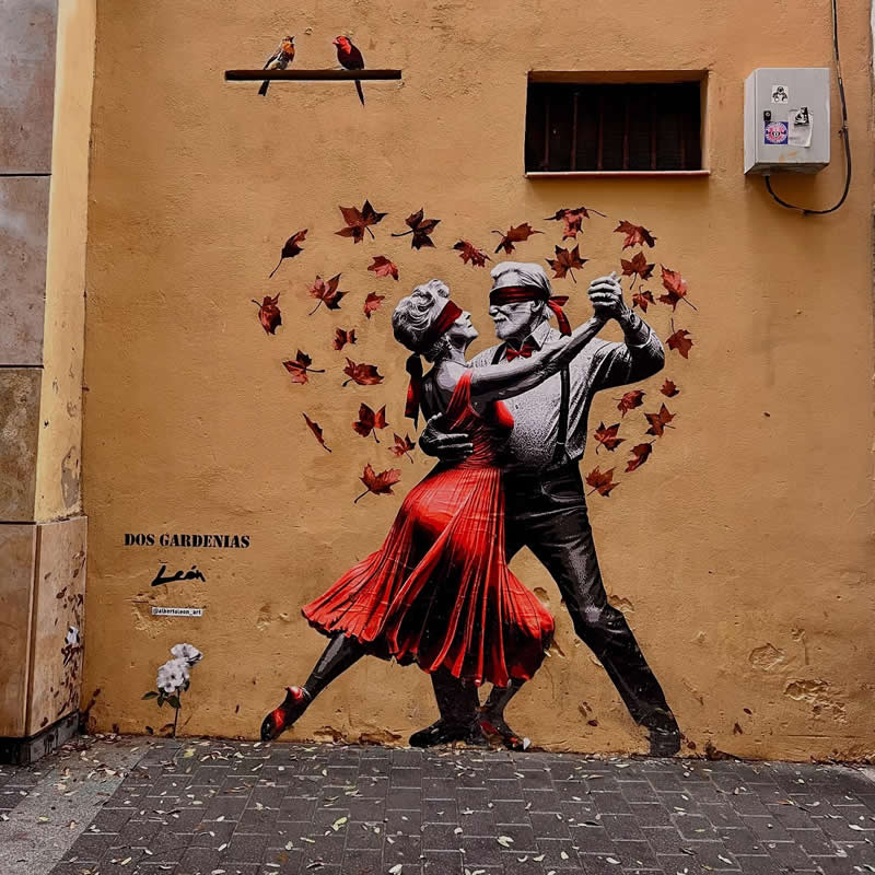A street mural shows an elderly couple dancing in tango style, both wearing blindfolds, with the woman in a flowing red dress and autumn leaves swirling around them on a warm-toned wall.