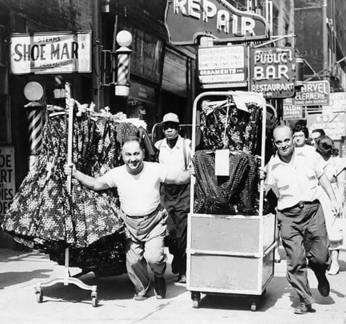 Men Pulling racks of clothing on a busy sidewalk in the Garment District, 1955.