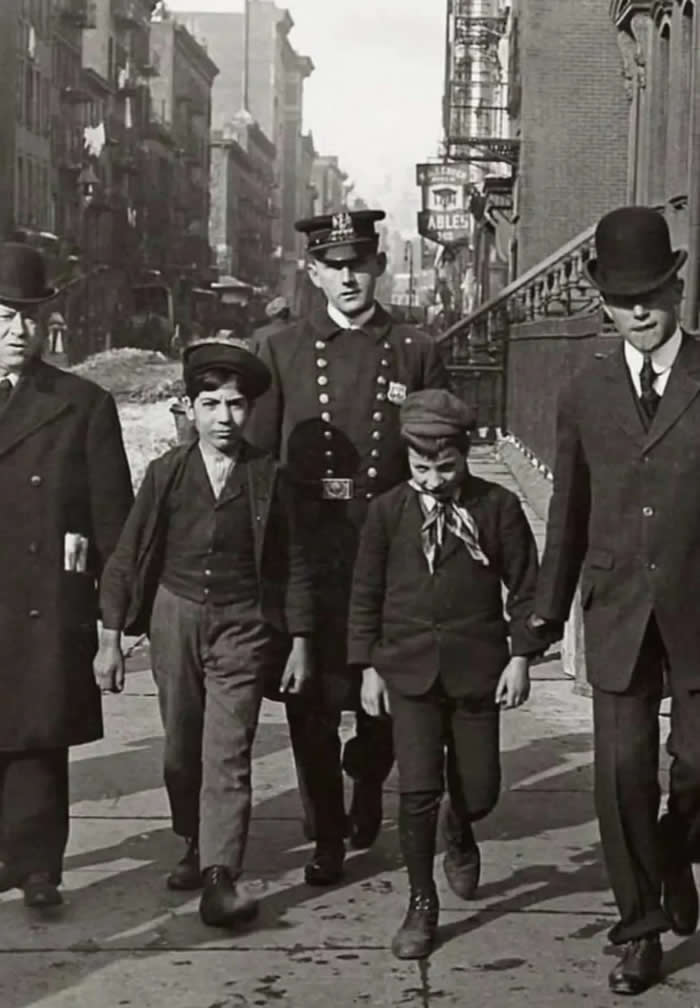 Two young boys are being arrested for pickpocketing on a bustling street in New York City. The boys were caught operating as a pickpocketing duo in Manhattan. Early 20th century.