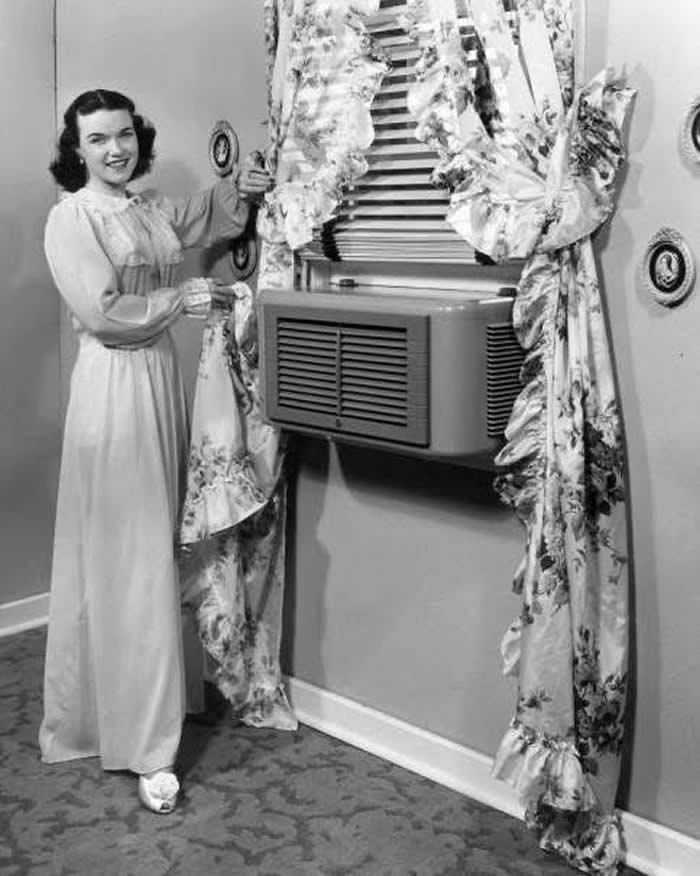 A woman showing her modern air conditioner mounted in the window, 1945