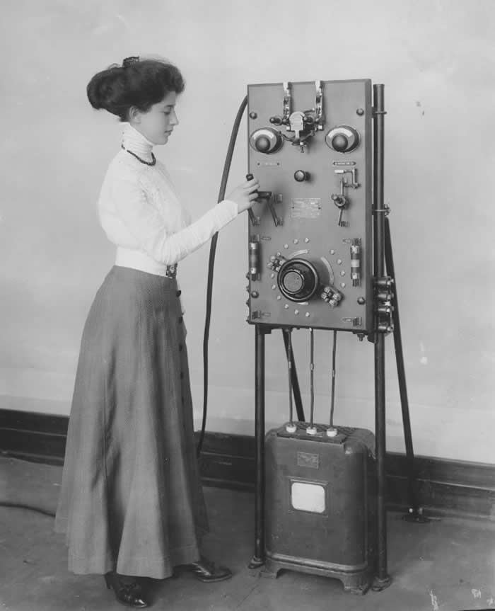 Woman posing with an early model of the GE electric charging station for electric cars, ca. 1912.