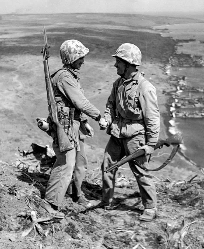 U.S. Marines, Cpl. Harold "Pie" Keller (right), shakes hands with Sgt. Howard Snyder (left), as they stand on the rim of Mt. Suribachi on Iwo Jima between the first and second flag raisings on February 23, 1945.