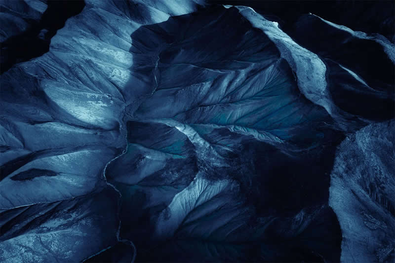 An aerial abstract view of Iceland's glacier featuring flowing blue ice formations, intricate frozen textures, and dramatic natural patterns that resemble a work of art.