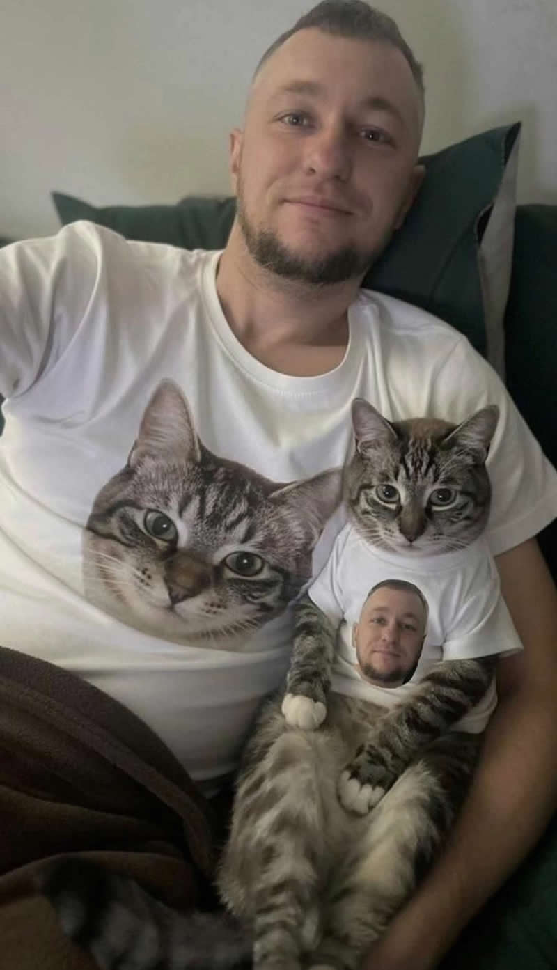 A smiling man and his tabby cat sit together wearing custom matching T-shirts. The man's shirt features the cat's face, while the cat's tiny shirt features the man's face, creating a hilarious and heartwarming fashion statement that perfectly celebrates their special bond.