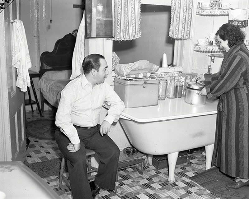 A woman fixing dinner on top of the bathtub, inside a tenement building on the Lower East Side, New York City in the 1940s.