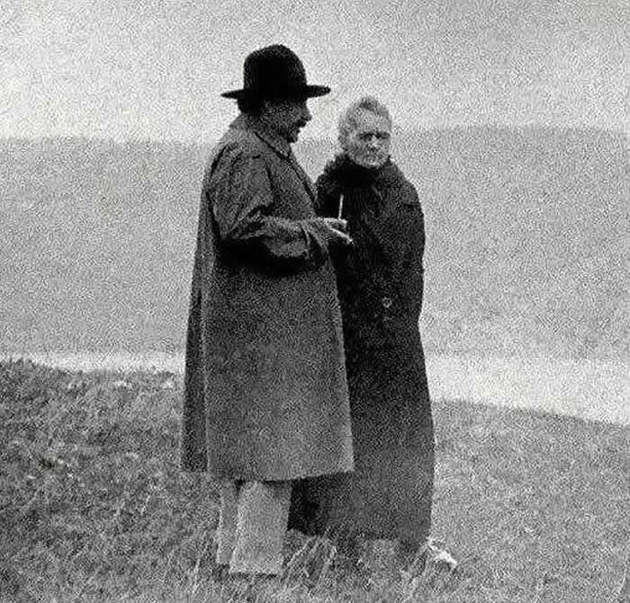Albert Einstein and Marie Curie discussing near a lake, 1929