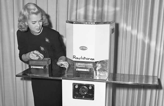 A woman demonstrating how to use the first commercial microwave oven called the Radarange, 1947. This was made by Raytheon.