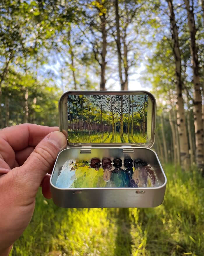 These 40 Tiny Altoid Tin Paintings by Remington Robinson Are Pure Pocket-Sized Magic 43 A hand holds an open Altoid tin in a sunlit forest, showing a miniature woodland painting by Remington Robinson inside the lid, with a tiny paint palette arranged in the bottom half.