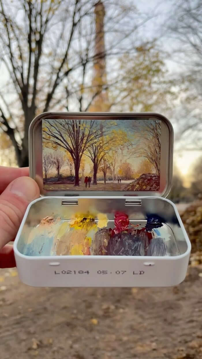 These 40 Tiny Altoid Tin Paintings by Remington Robinson Are Pure Pocket-Sized Magic 44 A hand holds an open Altoid tin outdoors, featuring a miniature autumn park painting by Remington Robinson inside the lid, while the bottom half contains a tiny oil paint palette with soft yellows, reds, blues, and grays.