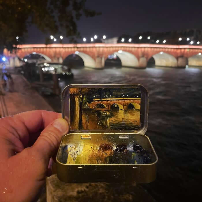 These 40 Tiny Altoid Tin Paintings by Remington Robinson Are Pure Pocket-Sized Magic 48 A hand holds an open Altoid tin beside a river at night, revealing a miniature painting by Remington Robinson of an illuminated bridge reflected in the water, with a tiny dark-toned paint palette arranged in the bottom half.