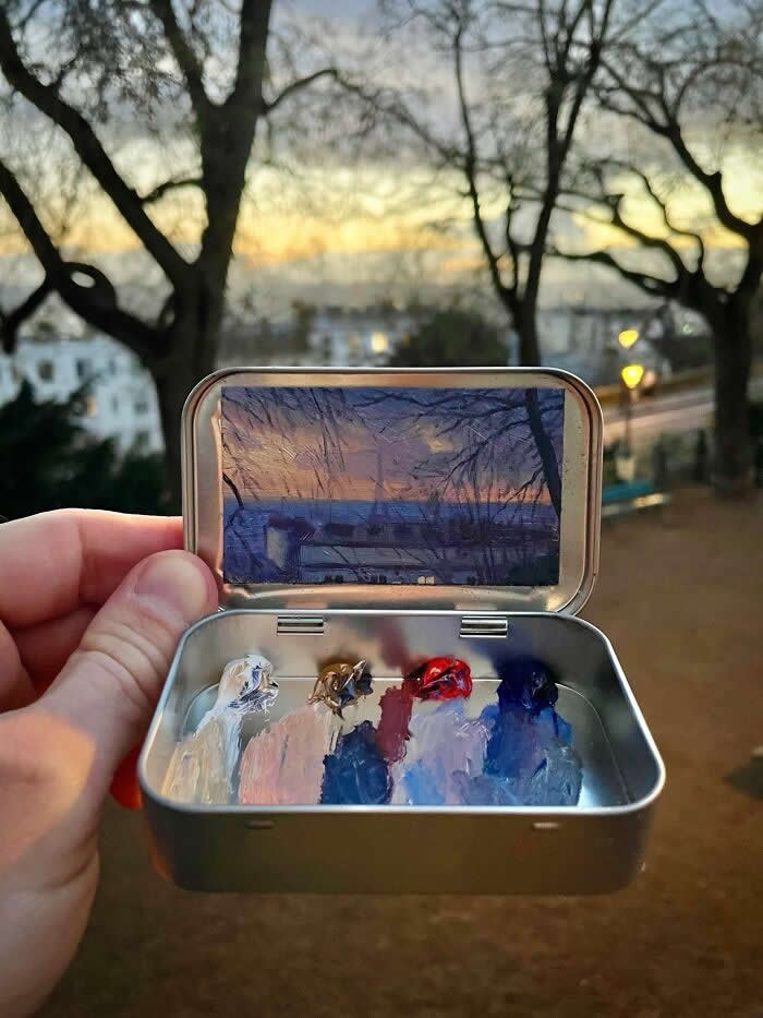 These 40 Tiny Altoid Tin Paintings by Remington Robinson Are Pure Pocket-Sized Magic 55 A hand holds an open Altoid tin at dusk, revealing a miniature painting by Remington Robinson of a quiet evening landscape framed by leafless trees, with a tiny paint palette of whites, blues, mauves, and warm earth tones in the bottom half.