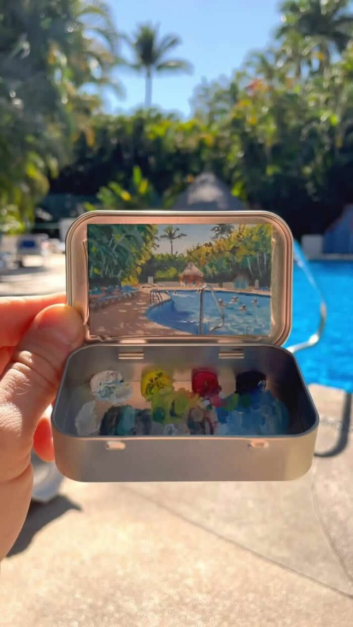 These 40 Tiny Altoid Tin Paintings by Remington Robinson Are Pure Pocket-Sized Magic 59 A hand holds an open Altoid tin beside a tropical swimming pool, revealing a miniature painting by Remington Robinson of a sunlit pool framed by palm trees and lush greenery, with a tiny paint palette arranged in the bottom half.