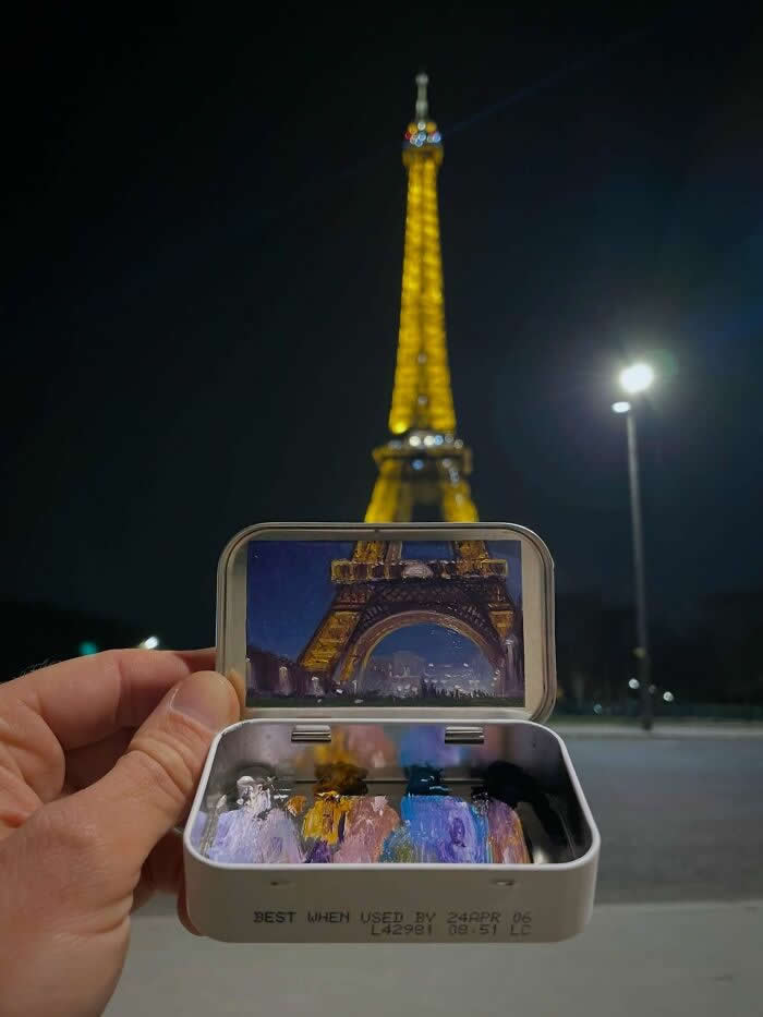 These 40 Tiny Altoid Tin Paintings by Remington Robinson Are Pure Pocket-Sized Magic 66 A hand holds an open Altoid tin at night in front of the illuminated Eiffel Tower, revealing a miniature painting by Remington Robinson of the tower’s glowing arch and the city lights beyond, with a tiny paint palette of gold, violet, blue, and black in the bottom half.