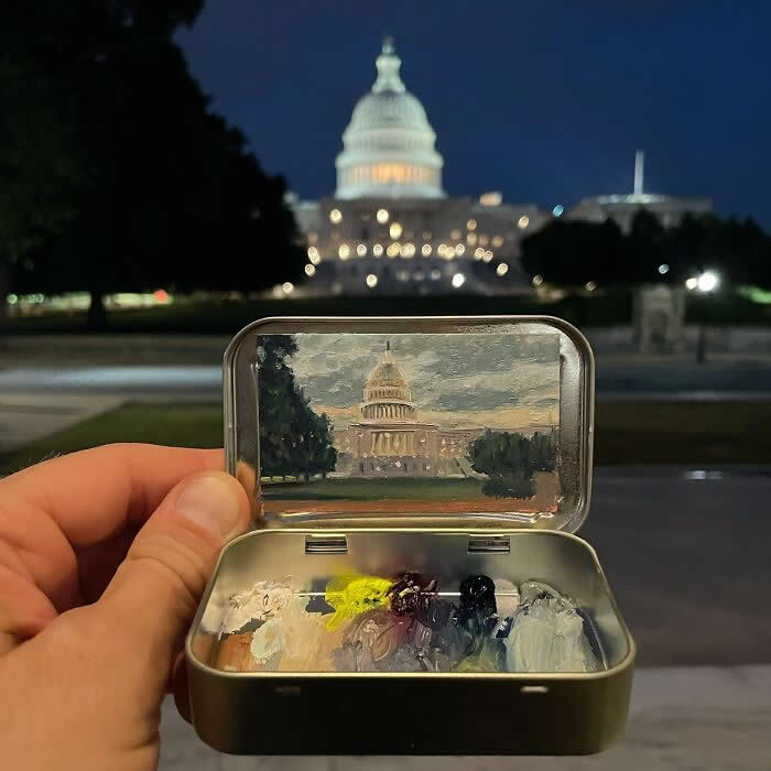 These 40 Tiny Altoid Tin Paintings by Remington Robinson Are Pure Pocket-Sized Magic 71 A hand holds an open Altoid tin at night in front of the illuminated U.S. Capitol, revealing a miniature painting by Remington Robinson of the domed building under a dusky sky, with a tiny paint palette of white, yellow, gray, and deep blue in the bottom half.
