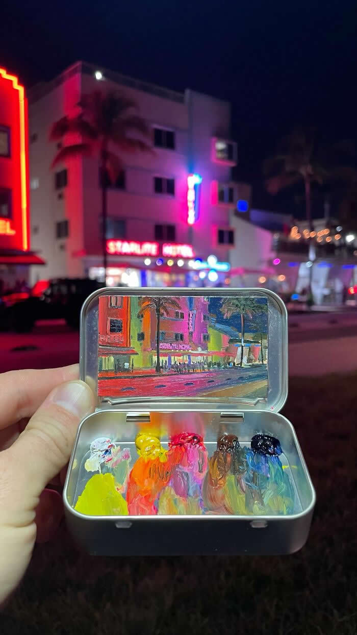 These 40 Tiny Altoid Tin Paintings by Remington Robinson Are Pure Pocket-Sized Magic 77 A hand holds an open Altoid tin at night in front of a neon-lit street scene, revealing a miniature painting by Remington Robinson of colorful Art Deco buildings, palm trees, and glowing hotel lights, with a vivid paint palette of yellow, orange, pink, brown, blue, and black in the bottom half.