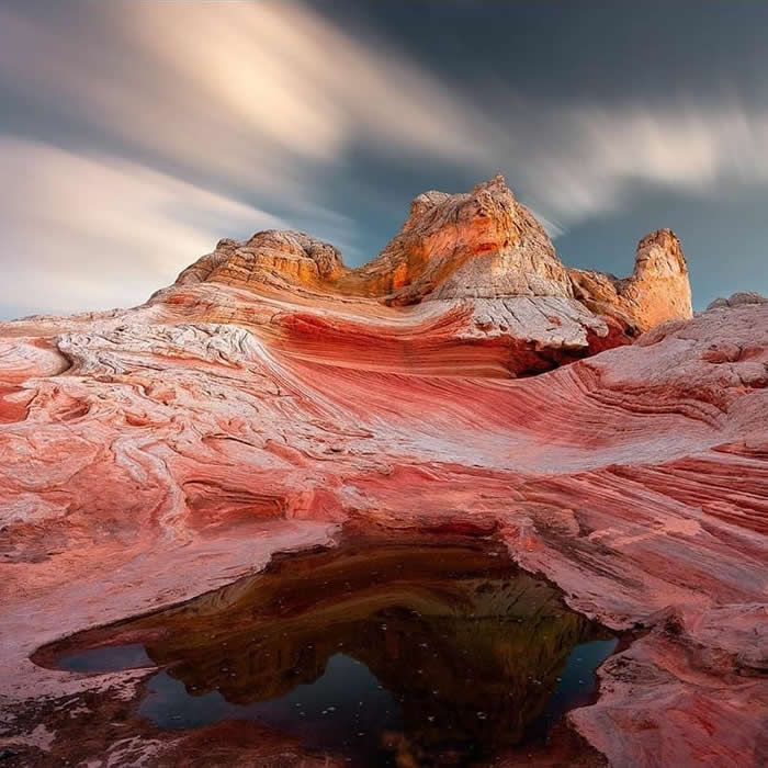 Beauty of the Earth: 33 Epic Landscape Views That Prove Nature Is the Greatest Artist 54 Layered red and white sandstone formations curve toward rocky peaks under a dramatic sky, with a dark reflective pool in the foreground adding depth to the desert landscape.
