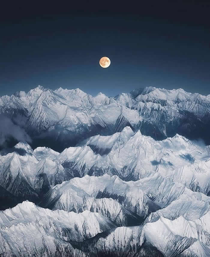 Beauty of the Earth: 33 Epic Landscape Views That Prove Nature Is the Greatest Artist 55 A full moon glows above a vast range of snow-covered mountain peaks under a deep blue night sky, with layered ridges stretching across the frame.