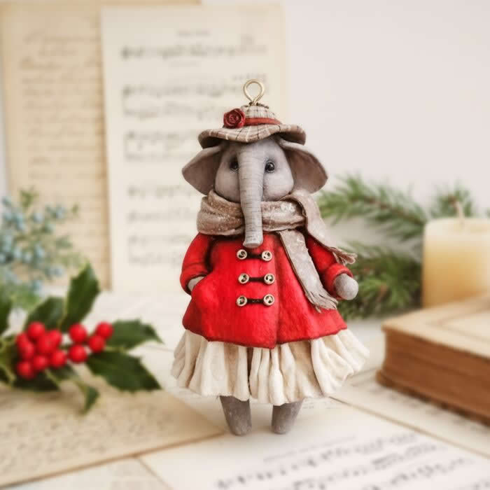 A handcrafted miniature elephant ornament made from cotton wool stands in a festive scene, wearing a bright red coat, pleated cream skirt, soft scarf, and tiny hat with a rose detail.