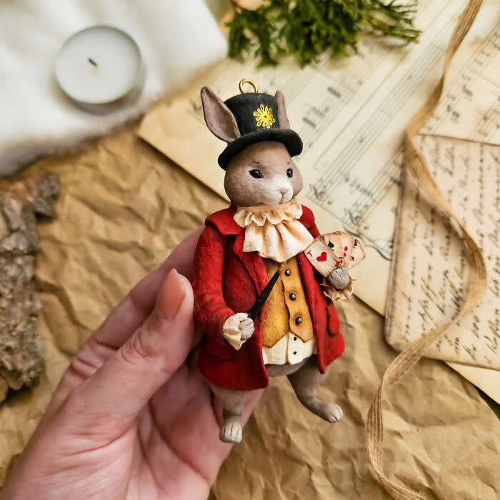 A handcrafted miniature rabbit ornament made from cotton wool wears a red coat, golden waistcoat, ruffled collar, and top hat while holding a tiny heart-themed card and wand against a vintage paper backdrop.