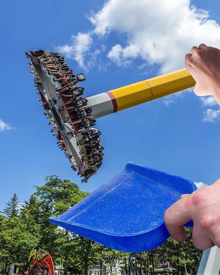A hand holds a yellow broom handle and a blue dustpan in the foreground, aligned with a spinning amusement park ride so the ride appears to be swept up like debris in a clever forced perspective illusion.