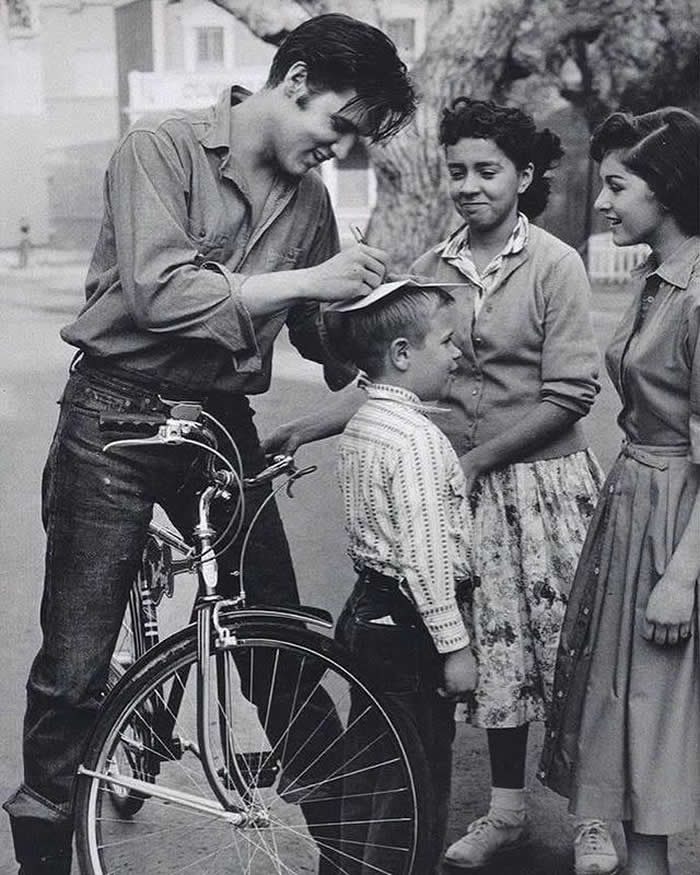 Elvis Presley signing autographs on top of a boys head, 1959