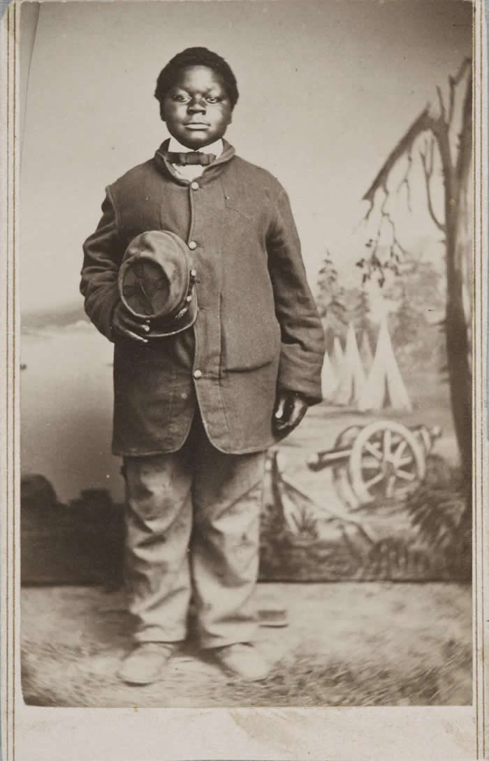 Civil war drumer boy posing on his uniform with his cap on hand, circa (1863)