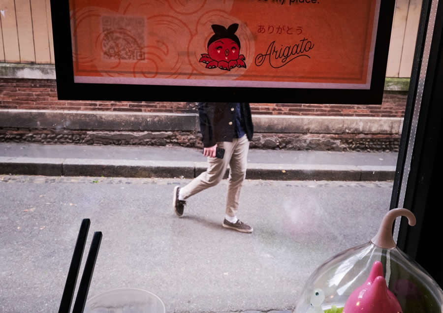 The Art of Perfect Timing: 34 Clever Street Photos by Emiliano Cuadrado That Turn Ordinary Scenes Into Visual Surprises 47 A pedestrian partially hidden behind a café window advertisement, with only the lower body visible, creating a playful illusion through layered framing and perfectly timed street photography.