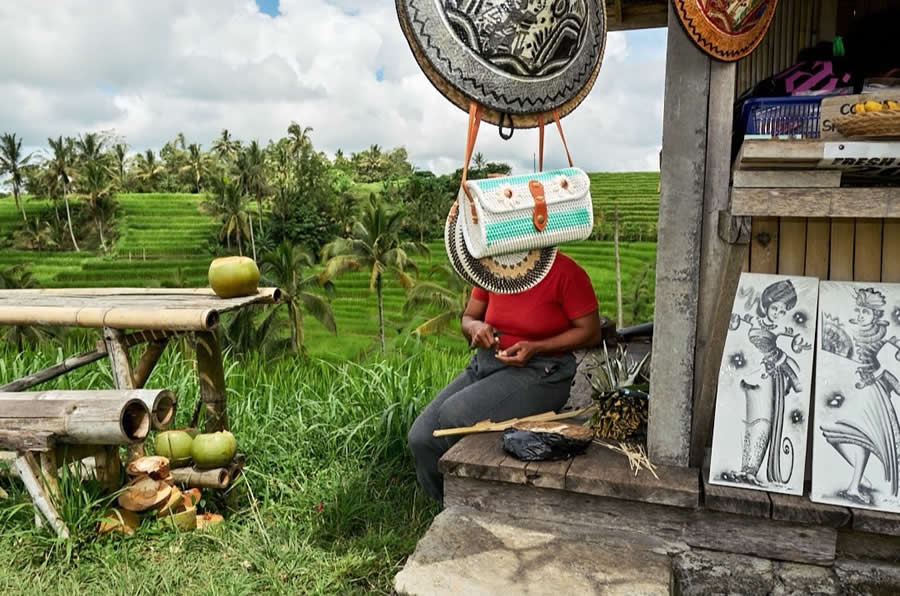 The Art of Perfect Timing: 34 Clever Street Photos by Emiliano Cuadrado That Turn Ordinary Scenes Into Visual Surprises 61 A seated vendor in a red shirt appears faceless as hanging woven bags perfectly align with the head, framed by lush green rice terraces and a rustic roadside market stall.
