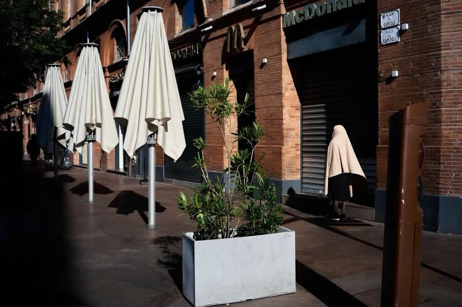 The Art of Perfect Timing: 34 Clever Street Photos by Emiliano Cuadrado That Turn Ordinary Scenes Into Visual Surprises 64 A pedestrian walking beside closed café umbrellas appears to become one of them through perfect alignment, creating a humorous optical illusion in a minimalist street photography composition.