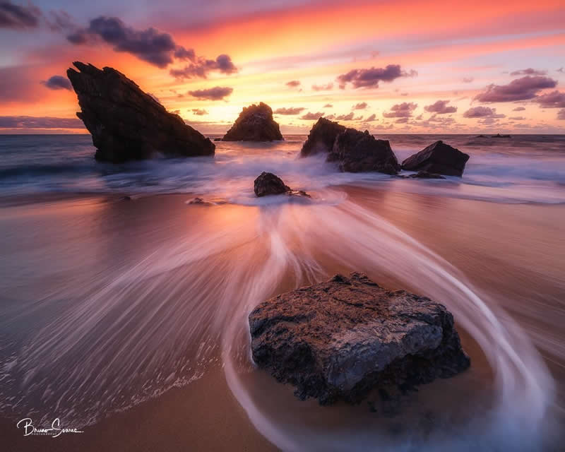 Solitary rock surrounded by ocean waves at sunset at Praia da Adraga, Portugal