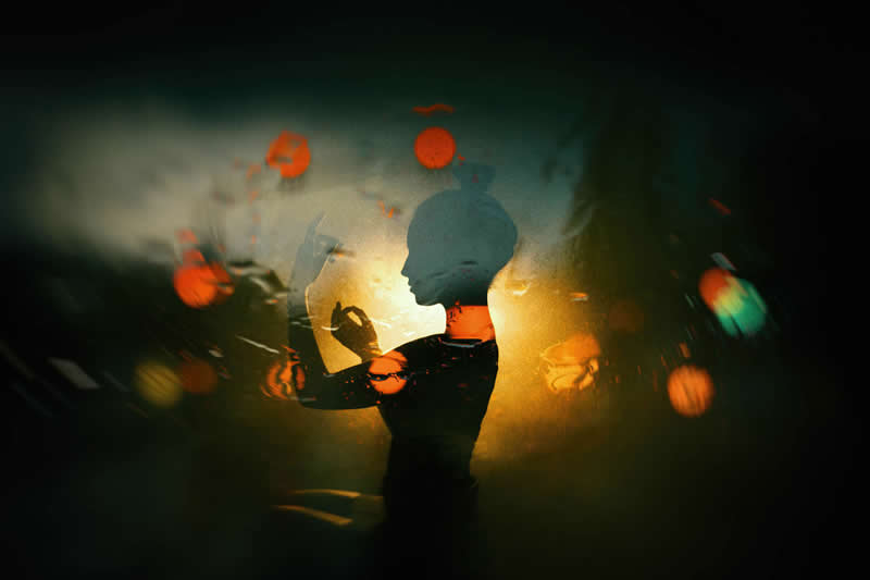 Cinematic portrait of a silhouetted person against a glowing golden light, surrounded by colorful reflections and motion blur in a dark, atmospheric setting.