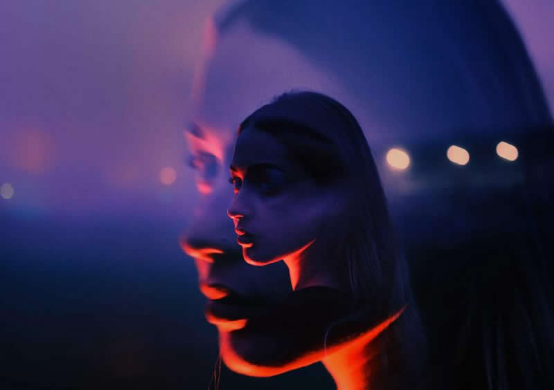 Cinematic double-exposure portrait of a woman in deep blue and purple light, with a larger translucent profile behind her and vivid red highlights along her face and neck.