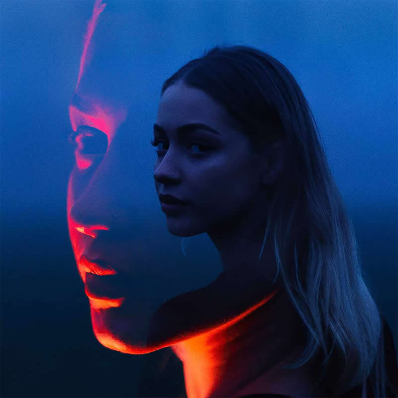 Cinematic double-exposure portrait of a woman in deep blue light, with a larger translucent profile beside her and vivid red highlights illuminating the reflection.