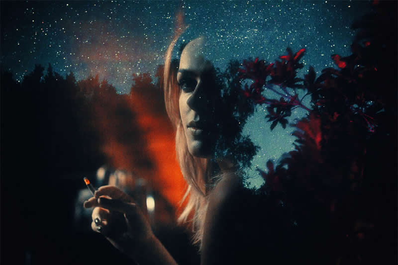 Cinematic double-exposure portrait of a woman holding a cigarette, layered with starry night skies, dark trees, and red foliage in an atmospheric composition.