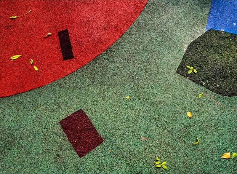 Abstract colorful surface featuring curved red, green, and blue shapes, dark geometric forms, and scattered yellow leaves creating a striking minimalist composition.