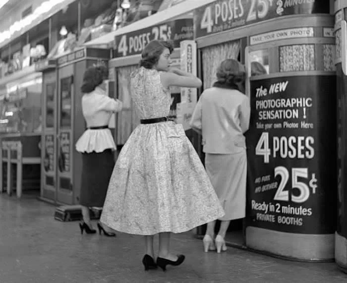 Selfies of 1954. Three young ladies preparing to have their pictures taken in a photo booth.