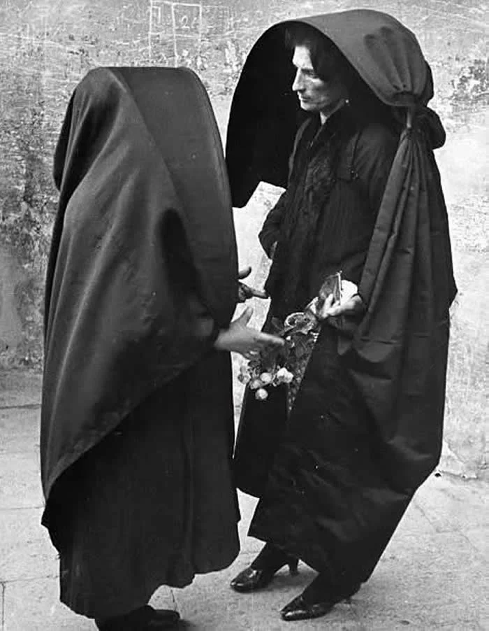 Two Maltese women talking. Malta (1950s). The ghonnella, sometimes referred to as a Faldetta, is a form of women's head dress and shawl, or hooded cloak, unique to the Mediterranean islands of Malta and Gozo. 
