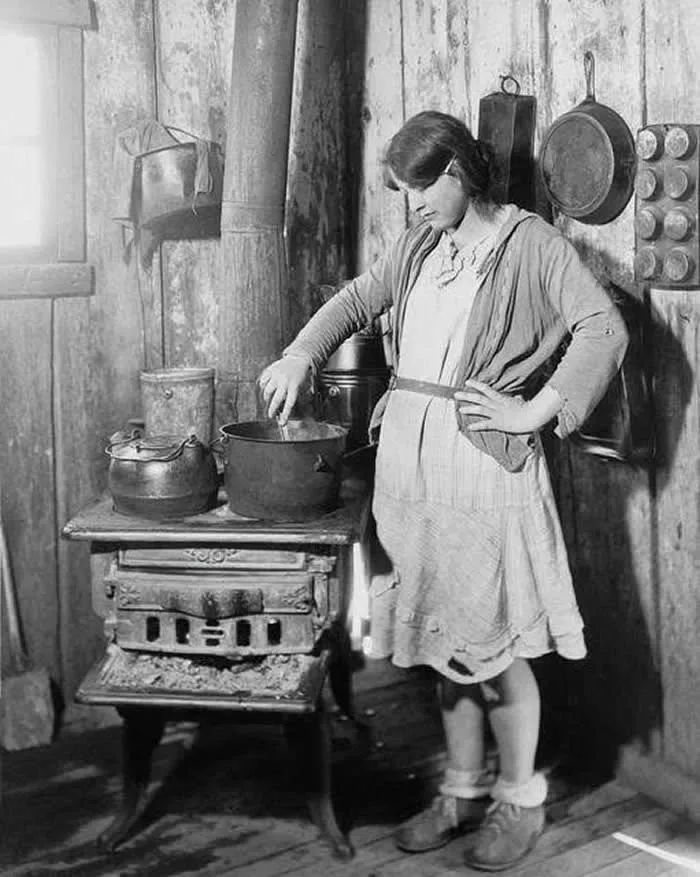 The teenage daughter of a an impoverished Arkansas farmer cooking on an old stove while her mother was in a tuberculosis sanitarium during the Great Depression. Red Cross photo from ca. 1930.