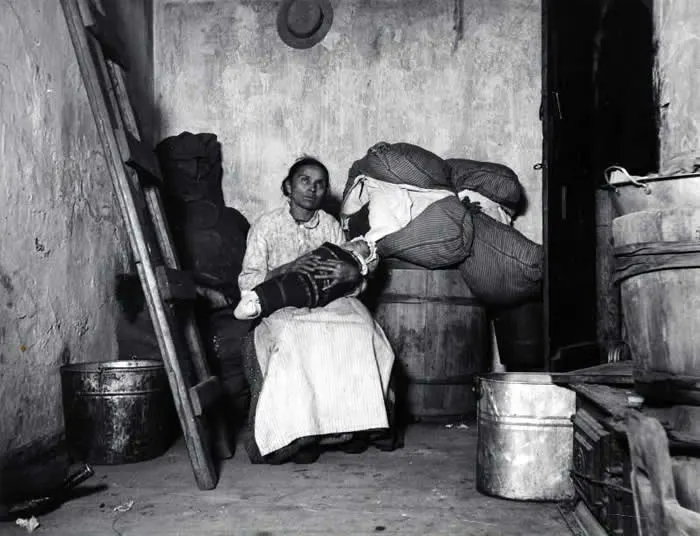 An Italian immigrant rag-picker sits with her baby in a small run-down tenement room on Jersey Street, 1887 (Photo by Jacob Riis).