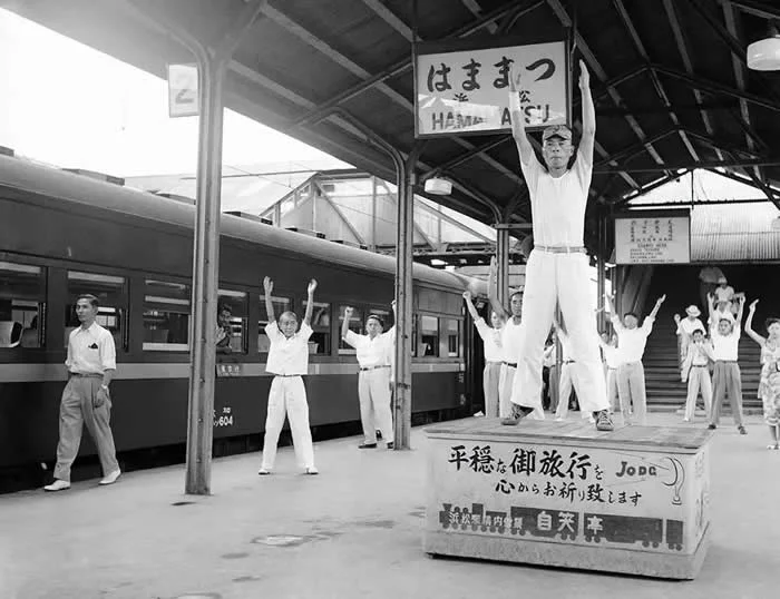 Passengers on a train traveling from Tokyo to Osaka go through three minutes of calisthenics under the leadership of a drillmaster, during a five-minute stopover at Hammamatsu on August 27, 1952.