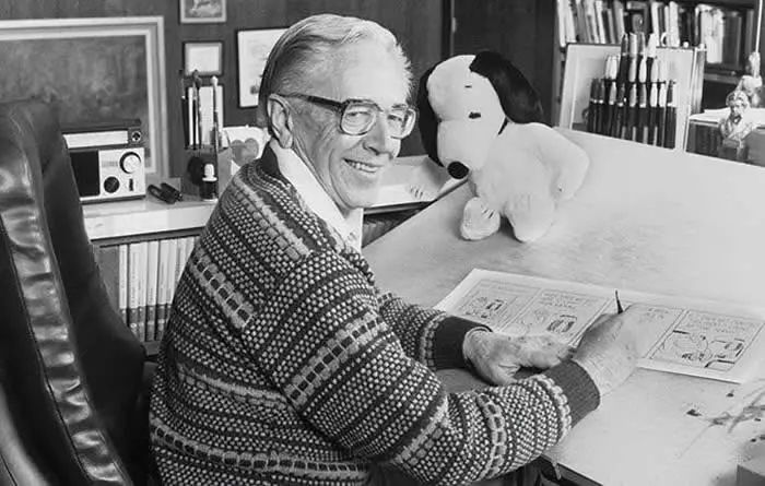 Cartoonist Charles M. Schulz drawing in his studio near a stuffed Snoopy toy, 1985