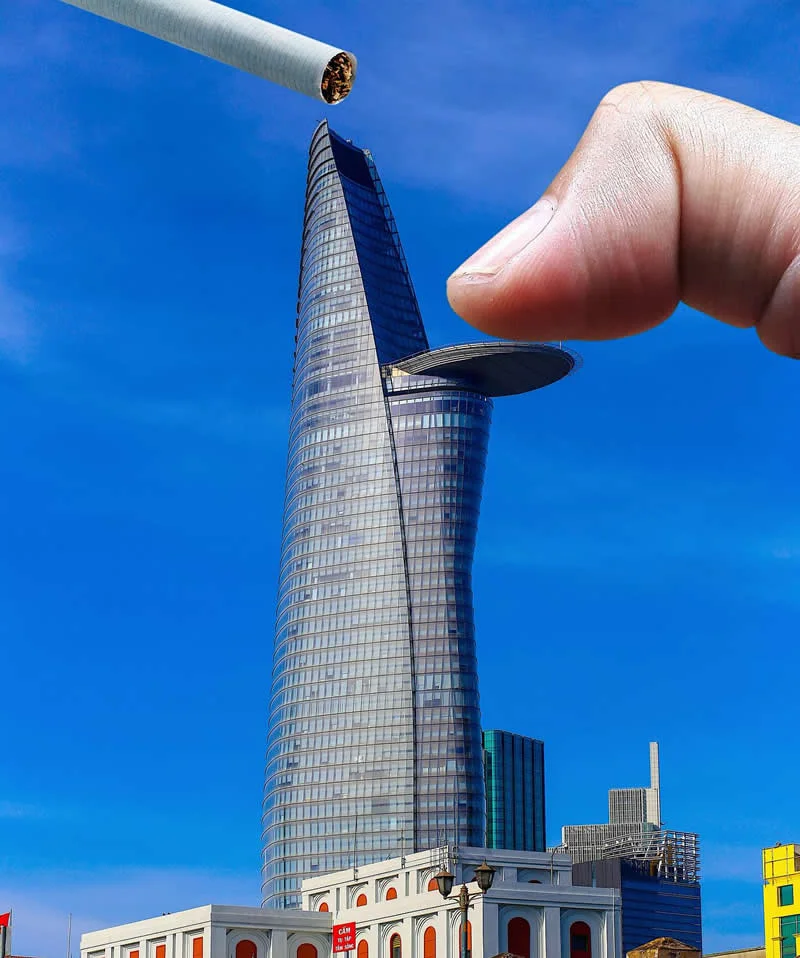 A large finger and a cigarette held in the foreground appear to pinch and extinguish a tall, curved glass skyscraper against a vivid blue sky. The building&rsquo;s projecting platform resembles part of the cigarette, creating a playful forced-perspective illusion.