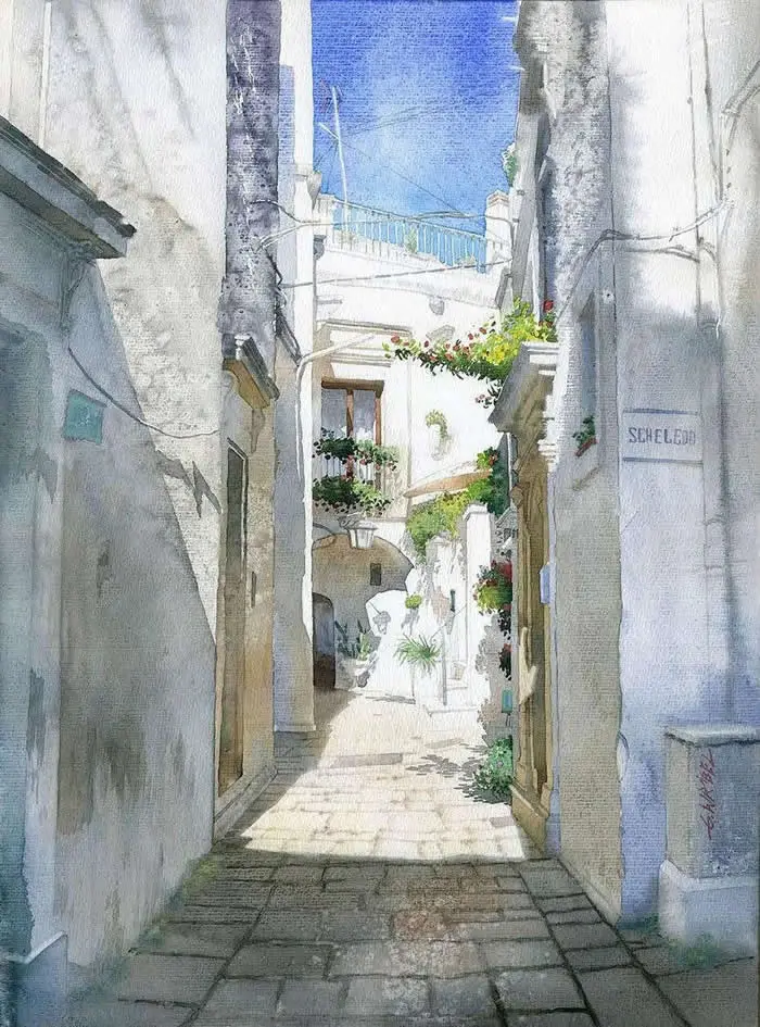 Watercolor painting by Polish artist Grzegorz Wr&oacute;bel depicting a narrow alley in Cisternino, Italy, lined with whitewashed buildings, stone paving, flower-filled balconies, and a bright blue sky overhead.