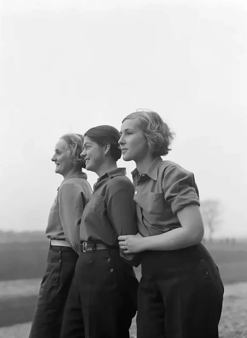 Willem van de Poll: The Master Photographer Who Captured a Changing World 41 Black-and-white photograph of three women standing arm in arm in an open field, wearing button-up shirts and dark trousers, with a wide, pale sky and distant countryside in the background.