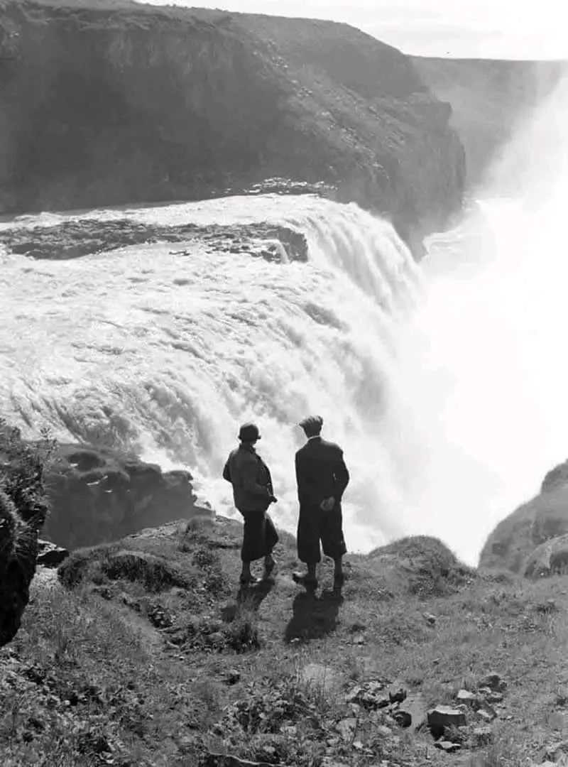 Willem van de Poll: The Master Photographer Who Captured a Changing World 46 Black-and-white photograph of two people standing on a rocky cliff overlooking a massive waterfall cascading into a deep gorge, surrounded by rugged cliffs, rushing water, and rising mist.
